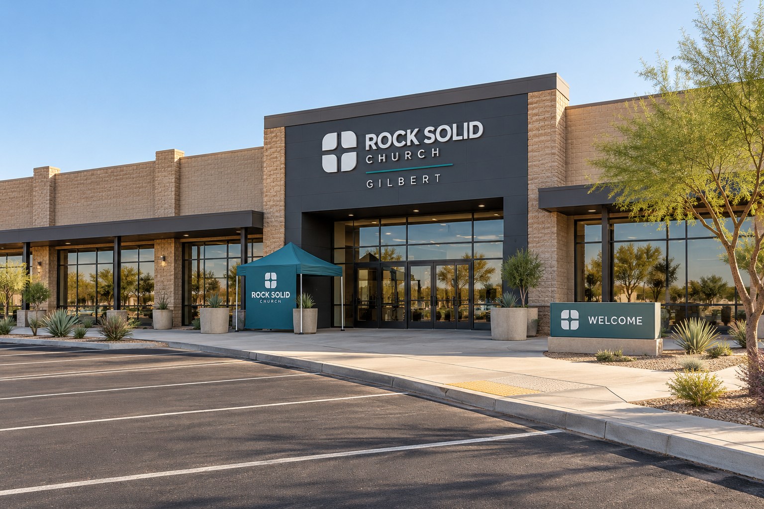 Gilbert's converted retail-anchor campus, with a broad brick storefront, glass entrance, portable welcome canopy, and clear parking approach.
